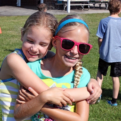 Two girls embrace in a hug outdoors at an O'Fallon Day Camp