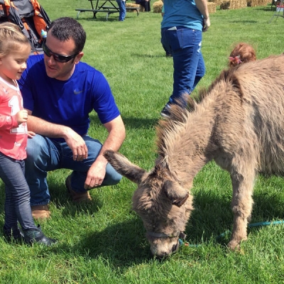 A daughter and father greet an animal at the Founders' Day petting zoo